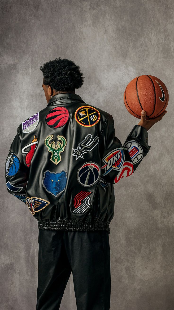 a man holding a basketball in his right hand and wearing a leather jacket with patches on it