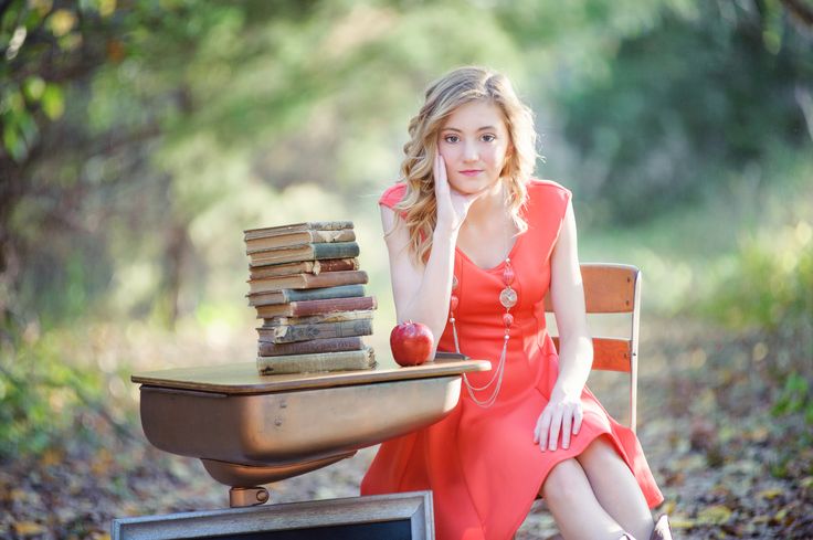 a woman sitting on a chair next to a pile of books with an apple in her hand