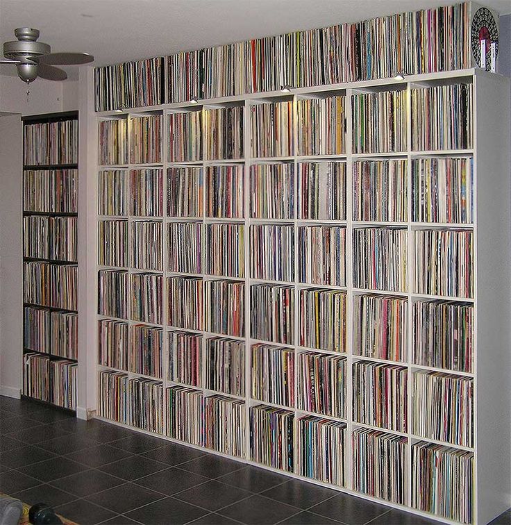 a room filled with lots of different kinds of records on the wall next to a ceiling fan