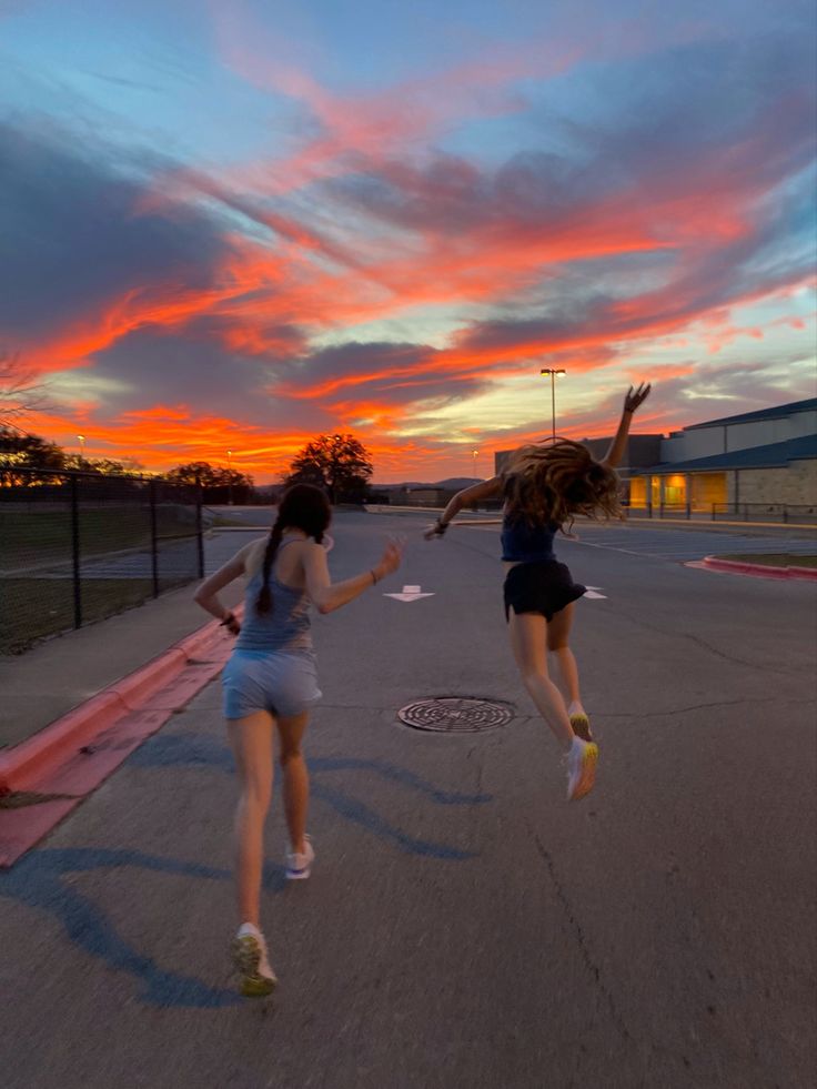 two girls are jumping in the air at sunset