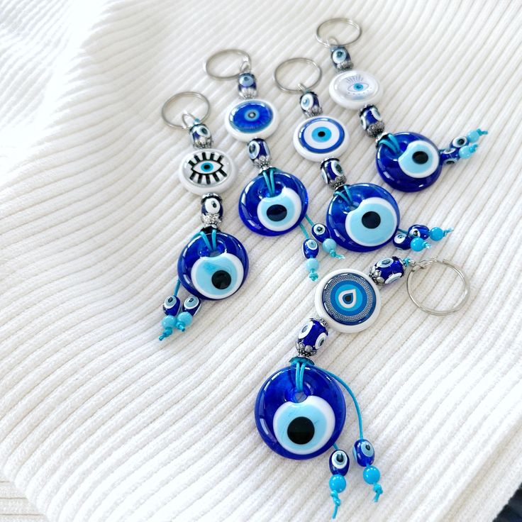 blue evil eye keychains are laying on top of a white sweater with beads