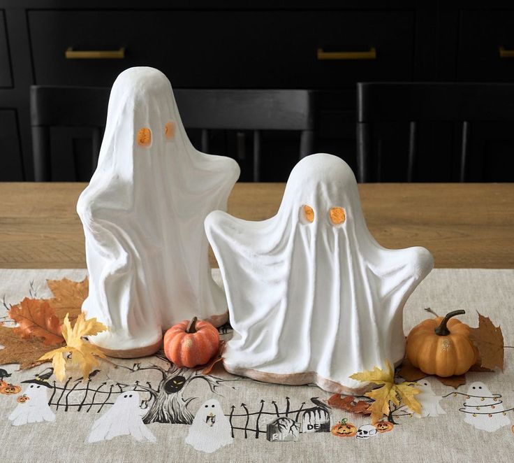 two white ghost figurines sitting on top of a table next to pumpkins