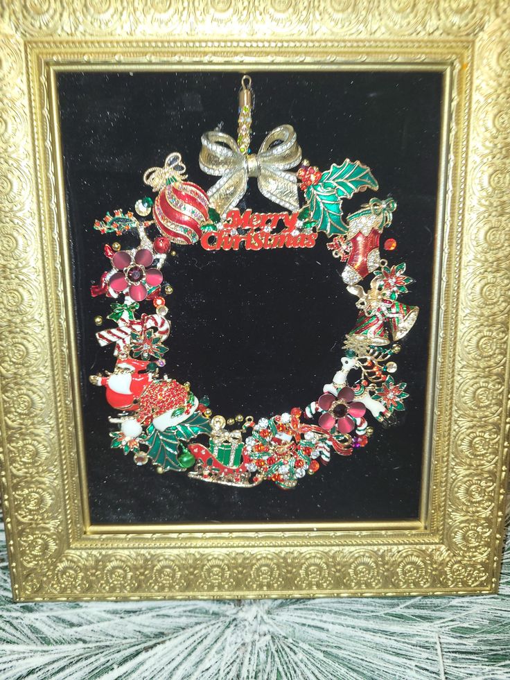 a framed christmas wreath with ornaments and bows on it in a gold frame, sitting on a table