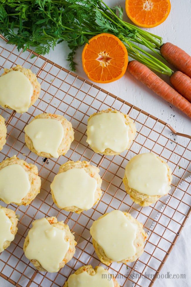 carrots and oranges are sitting on a cooling rack next to some frosted cookies