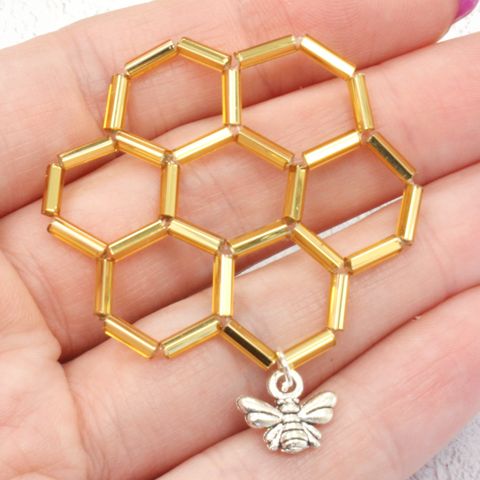 a gold honeycomb with a bee charm on it's end in someones hand