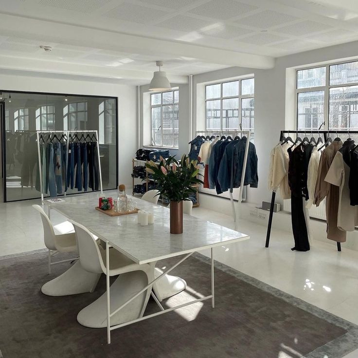 a clothing store with clothes hanging on racks and tables in front of them, all white