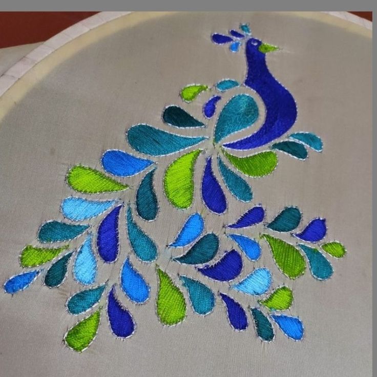 an embroidered peacock on a white cloth with blue and green leaves in the center, sitting on a table