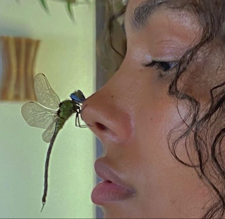 a close up of a person with a dragonfly on their nose and another insect sticking out of her mouth