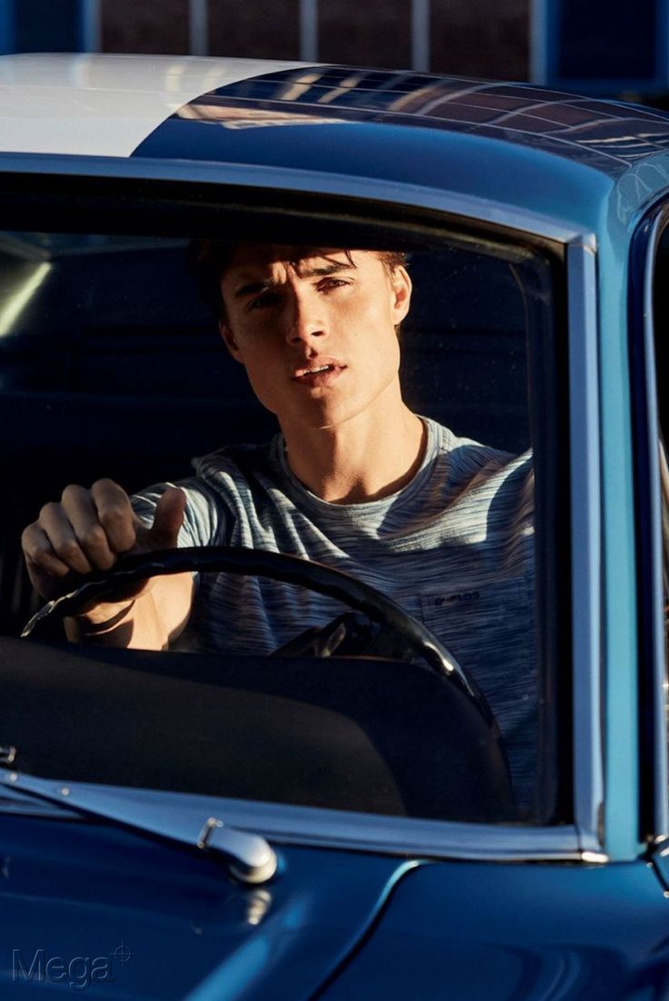 a young man driving a blue car with his hand on the steering wheel