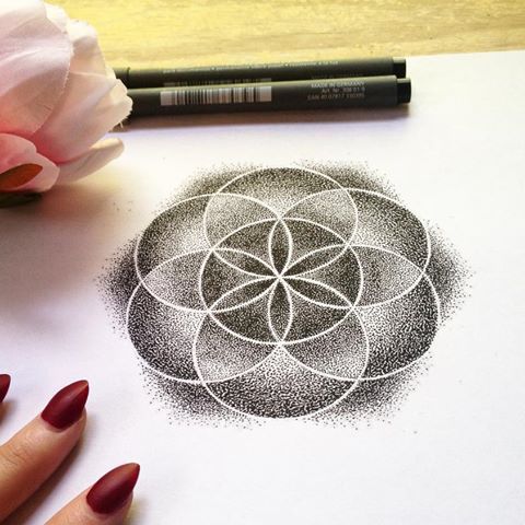 a woman's hand is drawing a flower on paper