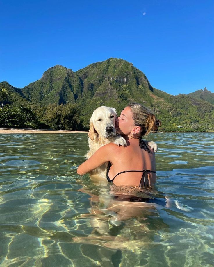 a woman and her dog are in the water with mountains in the backgroud