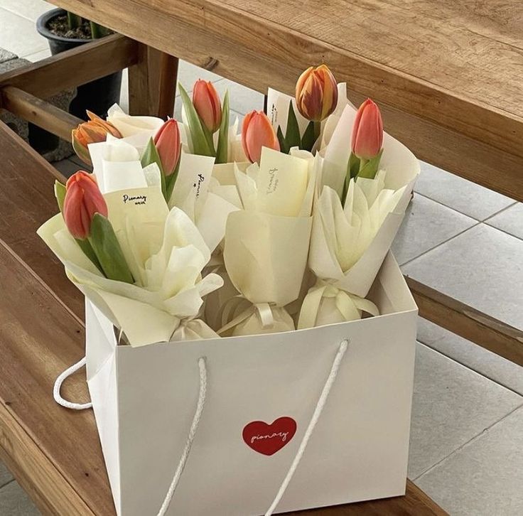 a bouquet of tulips in a paper bag on a bench