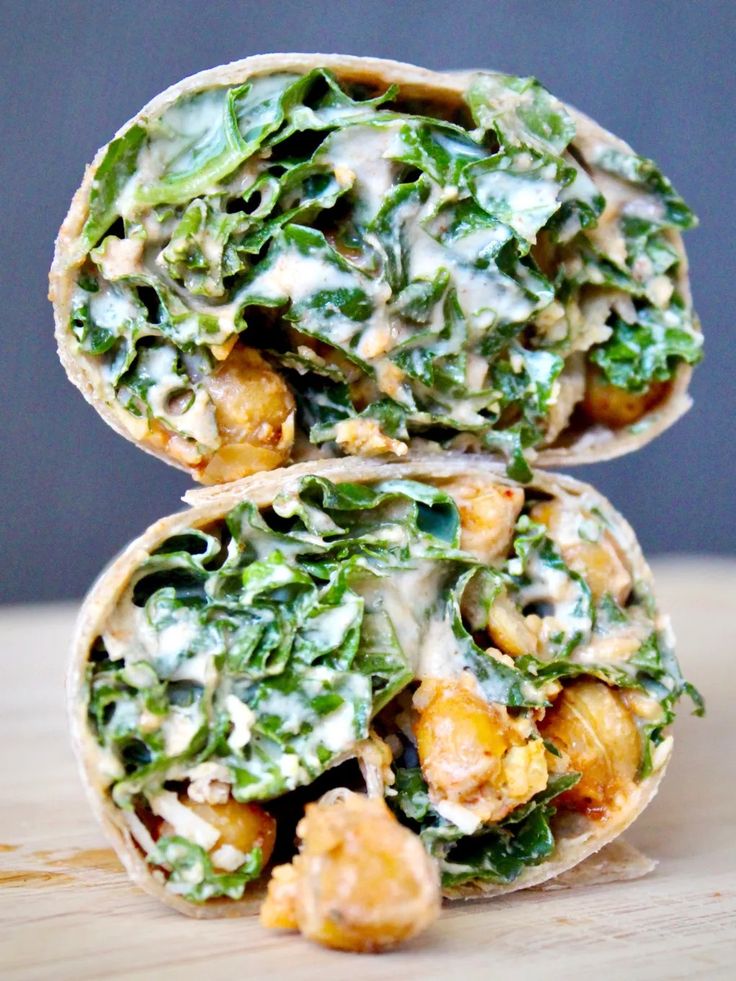 two wraps filled with greens and chicken on top of a wooden table