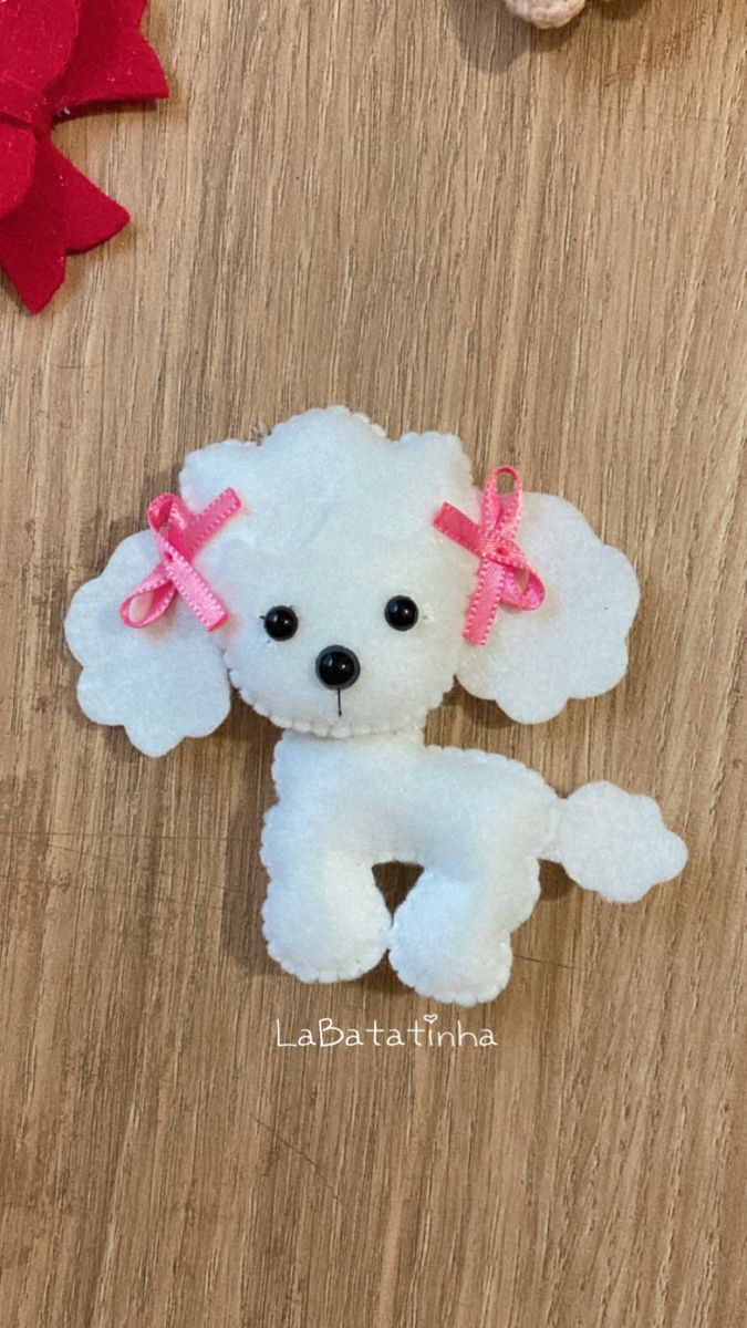 a small white dog with pink bows on its head sitting on a wooden table next to other stuffed animals