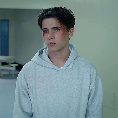 a young man in a grey hoodie is staring at the camera while standing in an empty room