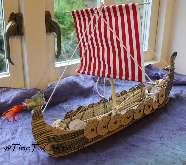 a wooden model of a boat on a purple bed with blue sheets in front of a window