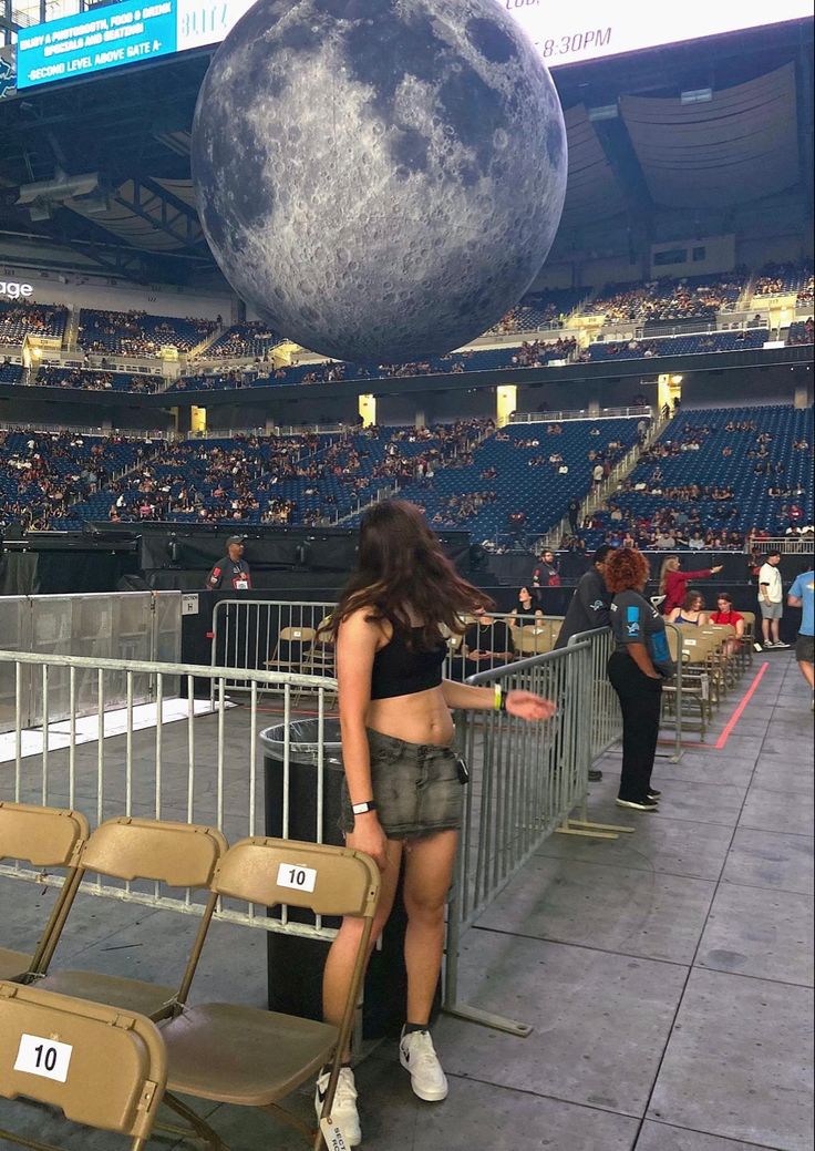 a woman standing next to a fence in front of a giant moon on top of a stadium