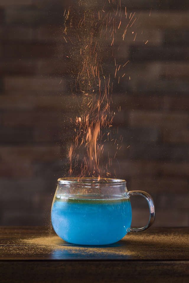 a blue liquid in a glass cup with fire coming out of it