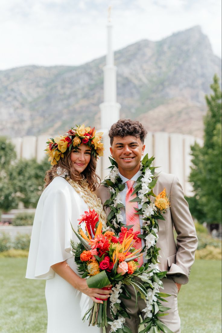 a man and woman standing next to each other in front of a church with flowers on their heads