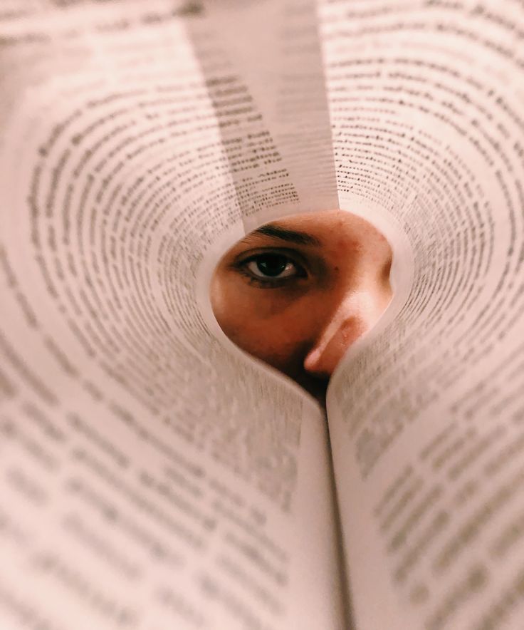 a woman's face peeks out from behind an open book with words on it