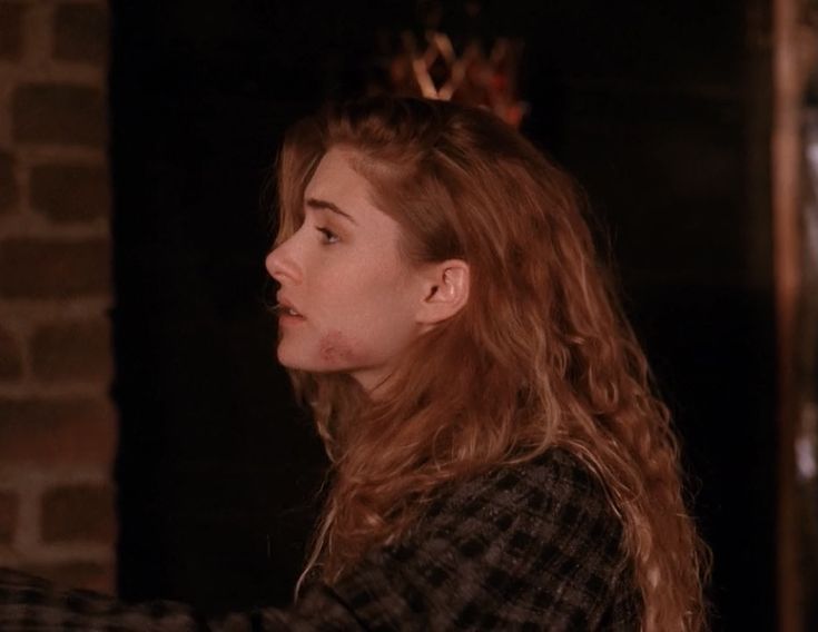 a woman with long hair standing in front of a brick wall