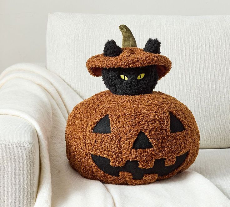 a stuffed pumpkin sitting on top of a white couch with a black cat in it's hat