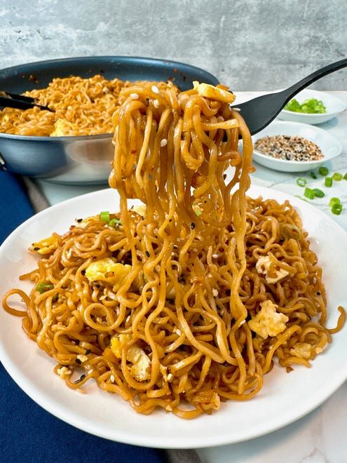 noodles being lifted from a pan with chopsticks over them on a white plate