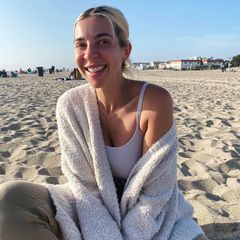 a woman sitting on the beach wrapped up in a towel and smiling at the camera