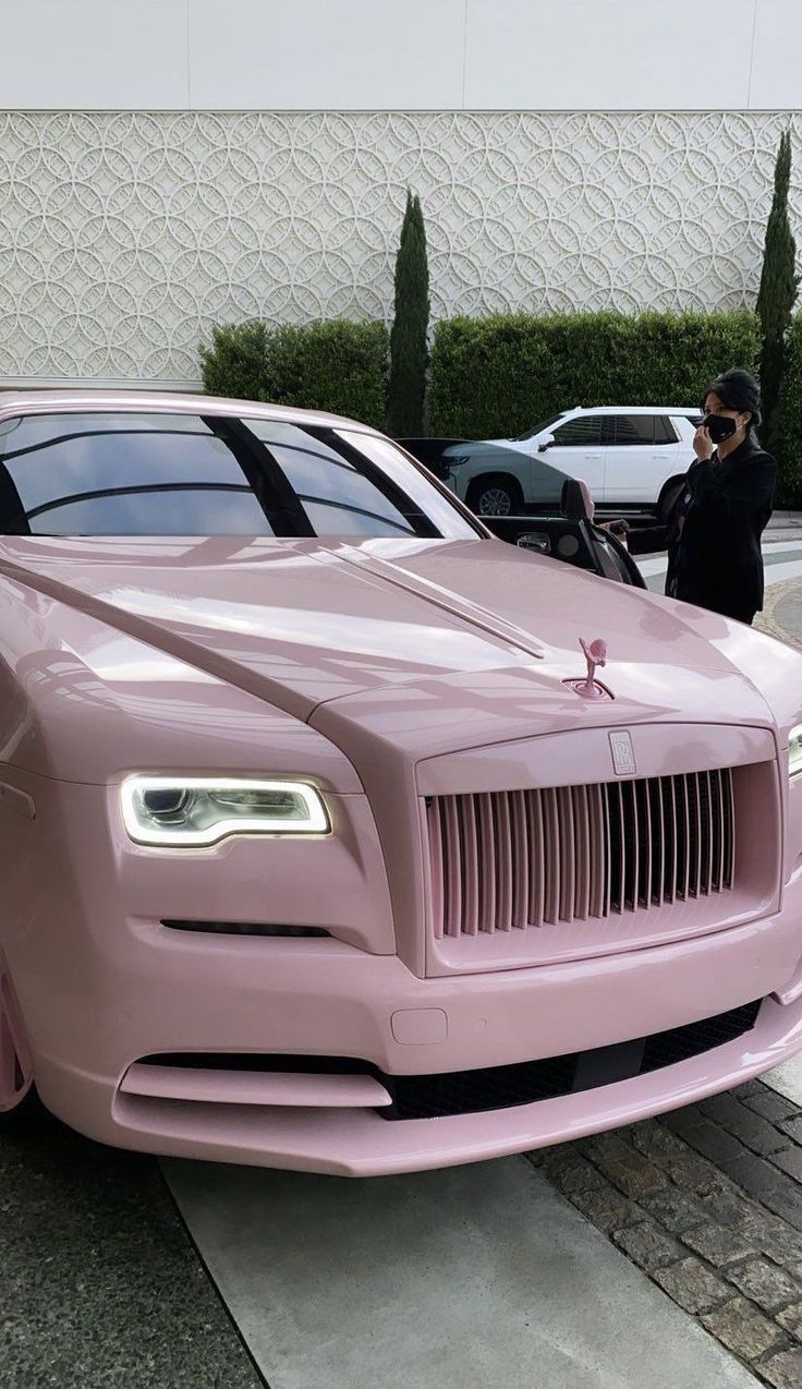 a pink rolls royce parked in front of a building with a woman taking a photo