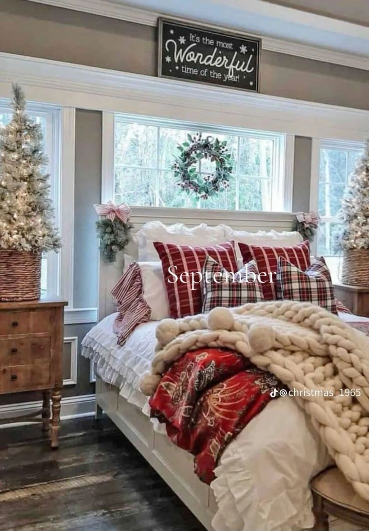 a white bed topped with pillows and blankets next to a window filled with christmas decorations