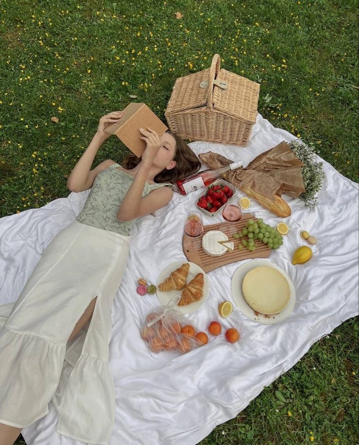 a woman laying on top of a white blanket next to a picnic table filled with food