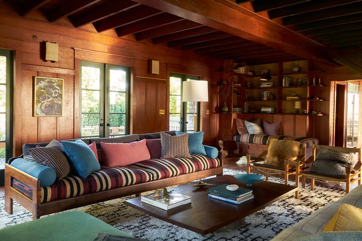 a living room filled with lots of furniture and wooden paneled walls covered in windows