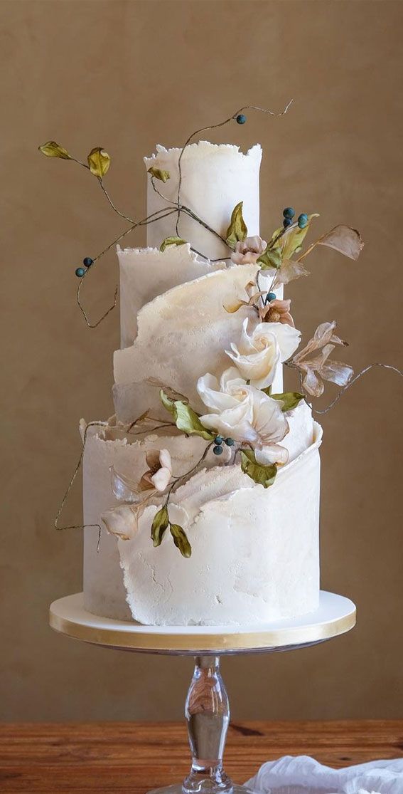 a three tiered white cake with flowers on top and leaves on the bottom, sitting on a wooden table