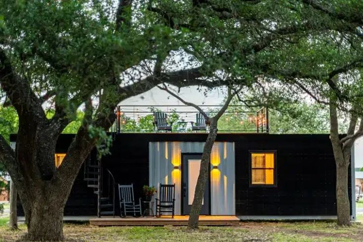 the tiny house is surrounded by trees and has yellow lights on it's windows