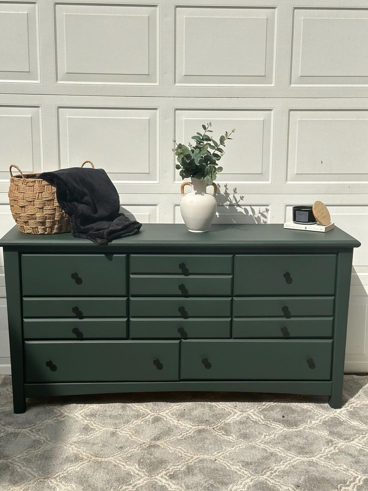 a green dresser sitting in front of a garage door next to a potted plant