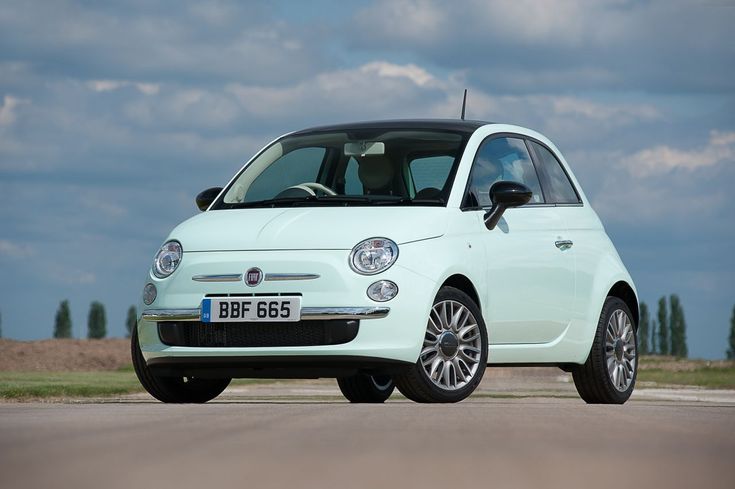 a small white car parked on the side of a road next to an empty field