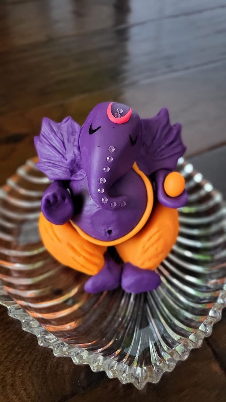 a purple elephant figurine sitting on top of an orange object in a glass bowl