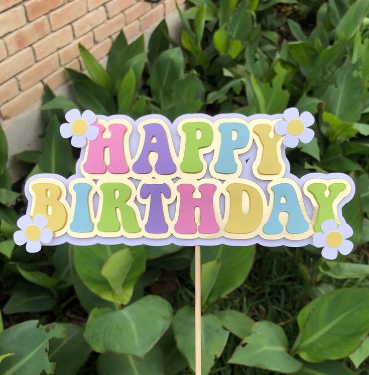 a happy birthday sign sitting on top of a wooden stick in front of some bushes