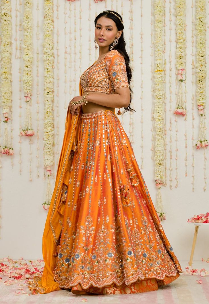 Editor's Note Rust Orange Mirror Thread And Zardosi Embroidered Raw Silk Lehenga. It Is Paired With A Matching Deep Neck Geometric Embroidered Blouse And Pure Silk Dupatta Fabric: Raw Silk, Silk Color: Rust Care: Dry Clean Only About the Designer Sanya Gulati's designs are inspired by the Indian bridesmaids, pastel easy hues & seasonal trends, her designs are a mix of modern, contemporary embroideries with traditional silhouettes thus creating our signature asymmetric checks embroideries amalgam Designer Orange Choli With Intricate Embroidery, Designer Wear Orange Choli With Intricate Embroidery, Chanderi Embroidered Sets For Reception, Dola Silk Floral Embroidery Set For Reception, Fitted Dola Silk Sharara With Floral Embroidery, Fitted Embroidered Orange Anarkali Set, Embroidered Sets For Diwali Reception, Orange Intricate Embroidered Sharara For Reception, Designer Embroidered Orange Blouse Piece