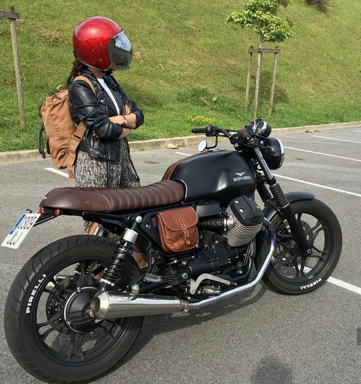 a woman wearing a red helmet standing next to a black motorcycle in a parking lot