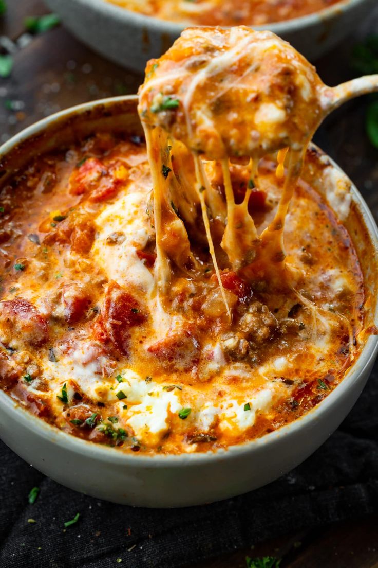 two bowls of lasagna with cheese being lifted from one bowl by a wooden spoon