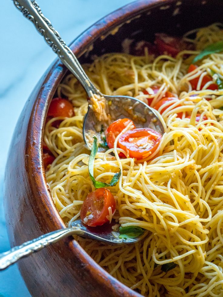 a wooden bowl filled with spaghetti and tomatoes