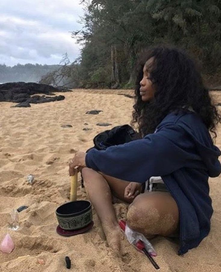 a woman sitting on top of a sandy beach next to a bucket and an umbrella