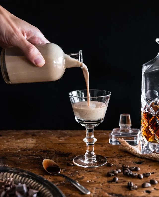 someone pouring coffee into a glass on top of a wooden table