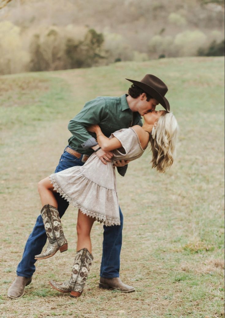 a man and woman are kissing in the middle of a field with cowboy boots on