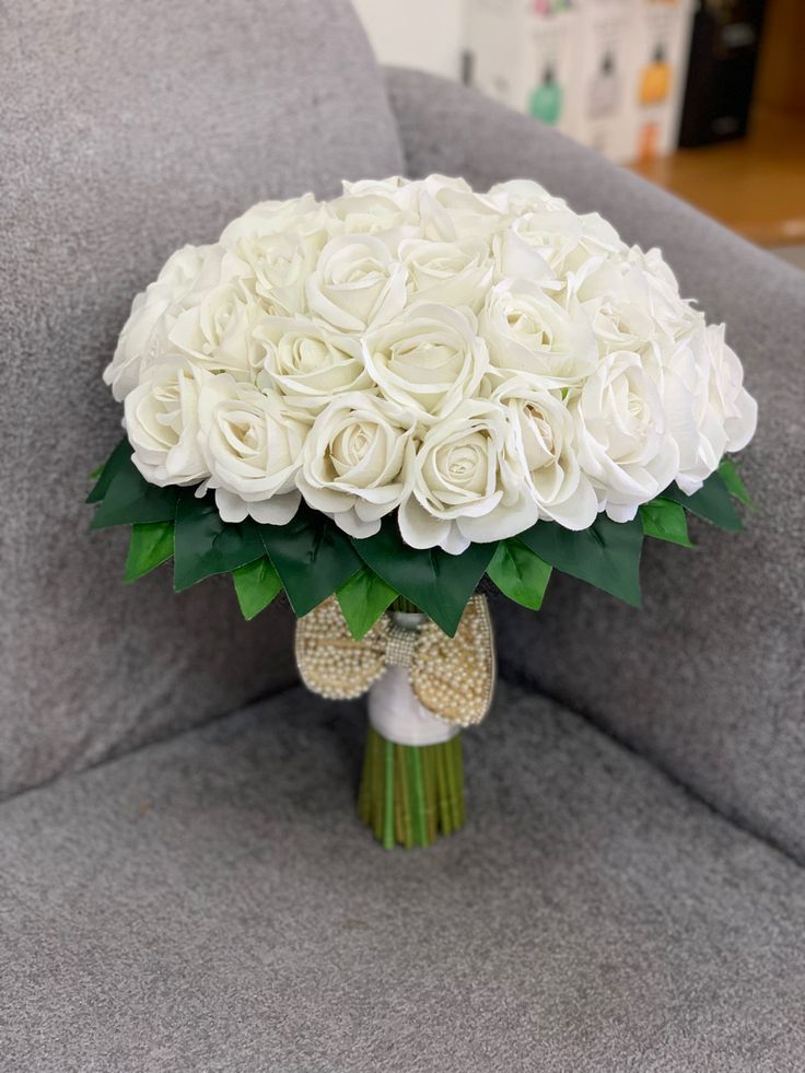 a bouquet of white roses is sitting on a gray chair in front of a wall