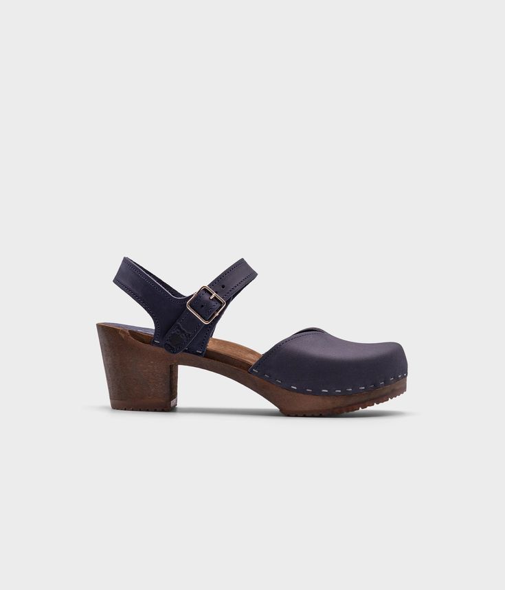 high heeled closed-toe clog sandal in navy blue nubuck leather stapled on a dark wooden base Classic Slingback Sandals With Heel Loop, Classic Ankle Strap Sandals With Rubber Sole, Classic Sandals With Reinforced Heel And Round Toe, Classic High Heel Sandals With Reinforced Heel, Classic Sandals With Heel Strap And Round Toe, Classic Open Heel Mules With Buckle Closure, Open Heel Heels With Rubber Sole And Medium Width, Medium Width Ankle Strap Heels With Rubber Sole, Open Heel Medium Width Heels With Rubber Sole