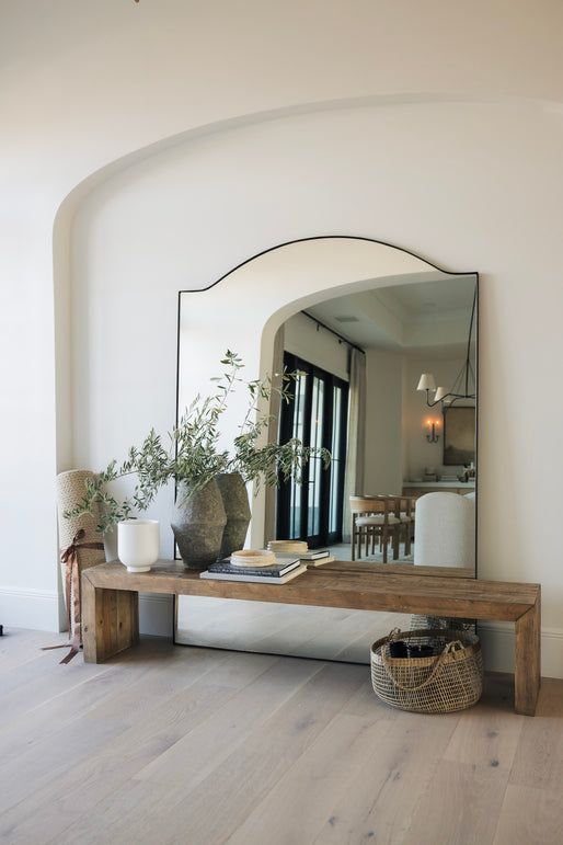 a mirror sitting on top of a wooden table next to a white chair and potted plant