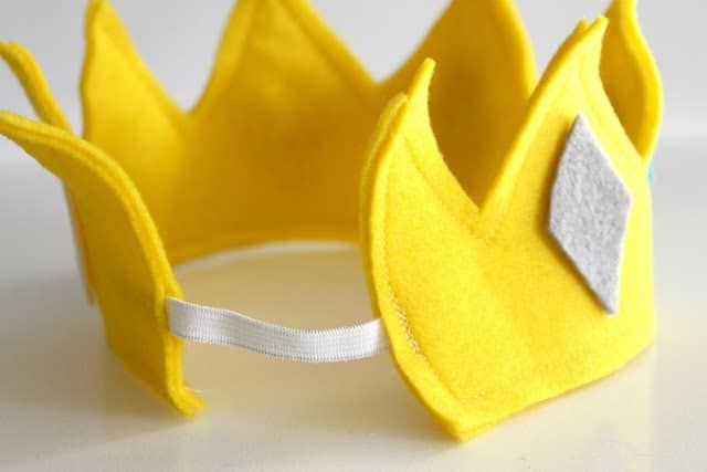 a close up of a yellow crown on a white surface with a ribbon around it