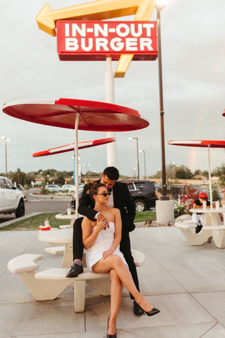 a man and woman are sitting on a bench in front of a burger restaurant sign